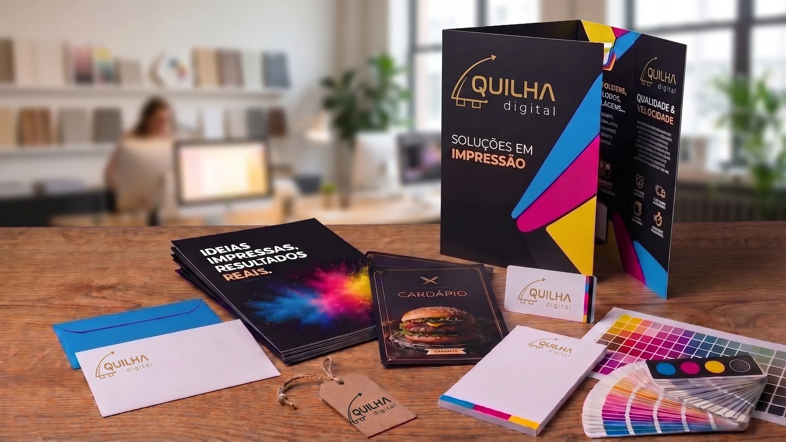 Peças impressas da Quilha sobre uma mesa de madeira: pasta com dobra, folhetos, cardápio, cartão de visita, envelope, etiqueta, bloco e leque de cores.